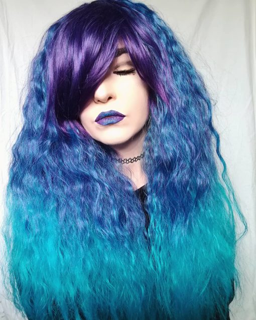 Purple and blue long wavy wig with bangs. Blueberry Fizz is a bursting concoction of colours. A purple fringe sits alone next to the sky blue roots that melts into an aqua ombre. The long thick fringe can be flipped to change up the look.