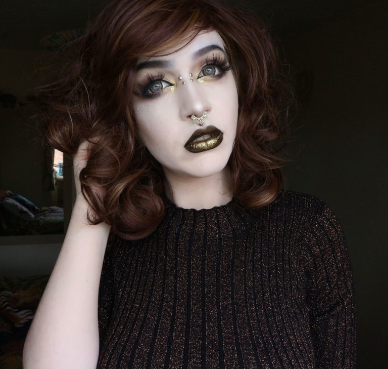 A warm brown wig with golden blonde highlights throughout. Styled into a long bob thats sleek from the roots, ending in large curls. The full blunt fringe is sleek.