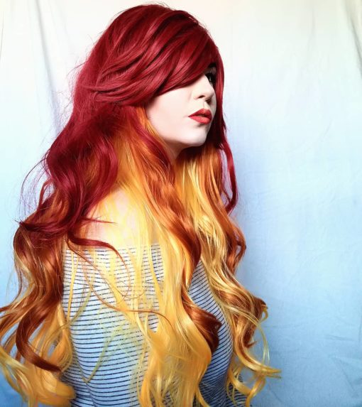 Flame - Lush Wigs UK Thick and bouncy, Flame has a deep red outer colour, and layers of yellow and orange hair underneath which peep through the lengths. It is styled in loose curls and has a heavy, side-swept fringe.