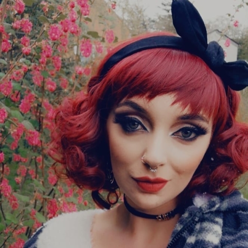 Red tinted short bob wig with bangs. Mademiselle is perfect for recreating hairstyles of the 1920s and 1930s retro era. A deep cherry red colour, in ringlet curls for glamour or loosened for a soft romantic vibe.