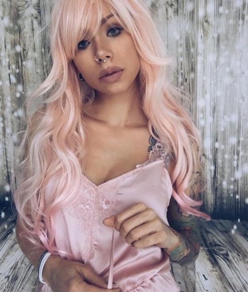 Pink long wavy wig with bangs. All things sweet go into Cutie Pie. The colour is a soft pastel peach shade with a mix of light pink running through. Finished with a baby pink dip dye on the ends.  
