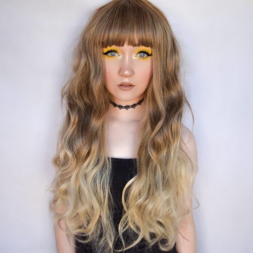 Dark blonde long wavy wig with bangs. Angelic hair is here! Hazel is a delicate ombre. Dark blonde roots melts into a light honey blond ombre, soft loose waves add volume.