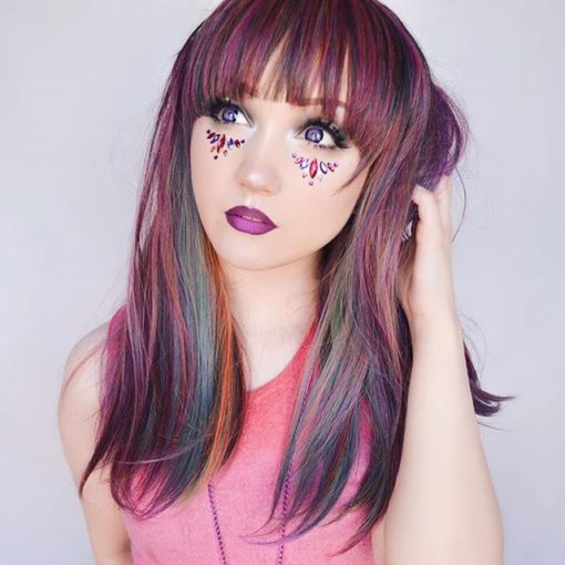 Multi colour long straight wig with bangs. Our dark side of the rainbow twist! A mixture of purples, pinks and green tones, blended with a deep red to bring it to life. Vivid colours transformed into muted tones.