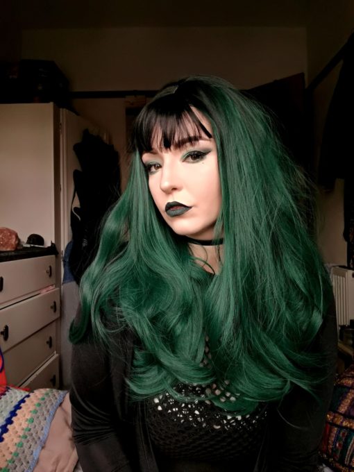 Green long curly wig with bangs. Deep forest green loose curls that fall to the waist, with an unusual twist! This sultry style has dark roots and a dark blunt fringe. The fringe is wispy and long enough that it could be swept over to one side.