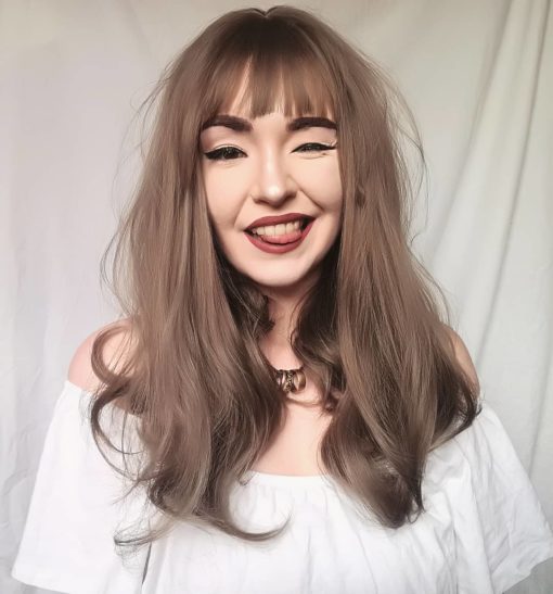 Grey long wig with bangs. Smoke Adds a natural and radiant look. Light sandy tones create this soft look. A delicate wave ends in a large curl at the ends.