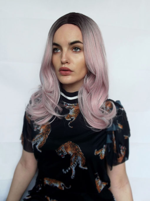 One of our fringeless pink styles with dark brown shadowed roots for a natural feel. A soft pink colour. The classic centre part is sleek from the roots and styled into curls.