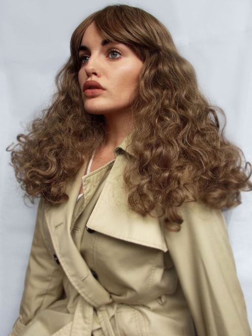 Brown curly long wig with bangs. Inspired by the 1970s disco era Echo has tight curls, curtain bangs, in a light chestnut colour. It's studio 54 again!