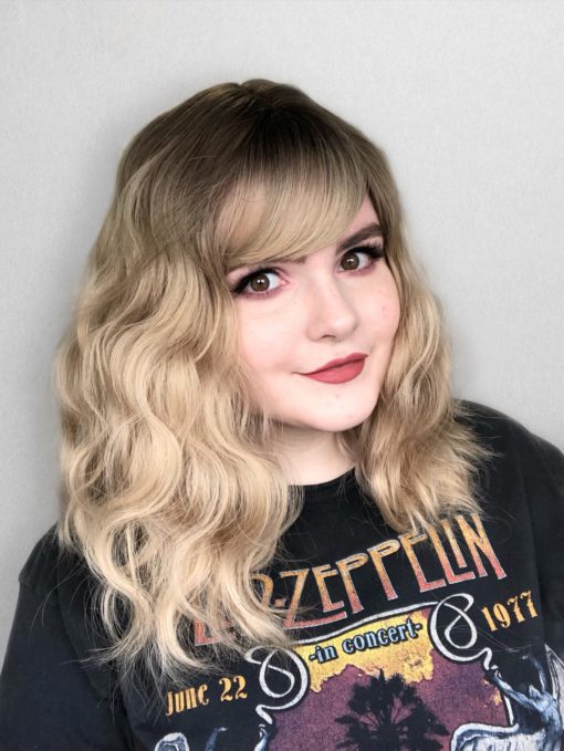 Blonde wavy long wig with bangs. Want a casual everyday style that meets your hair goals? Eleri makes a statement without even trying. Brown shadow roots blend into a wavy light blonde hue.