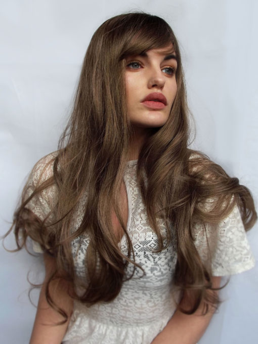 Dark blonde long curly wig with bangs. Willow doesn't fail when it comes to 70s hair. Soft and natural with a combination of dark blonde and light brown shades with dark brown shadowed roots. 