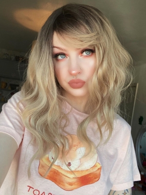 This long bob with dark brown shadow roots blend into a warm blonde hue. Styled in a loose wave with a sleek blunt fringe.