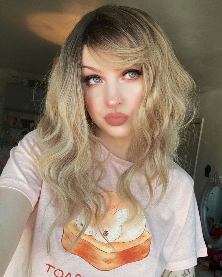 Eleri - Lush Wigs UK This long bob with dark brown shadow roots blend into a warm blonde hue. Styled in a loose wave with a sleek blunt fringe.