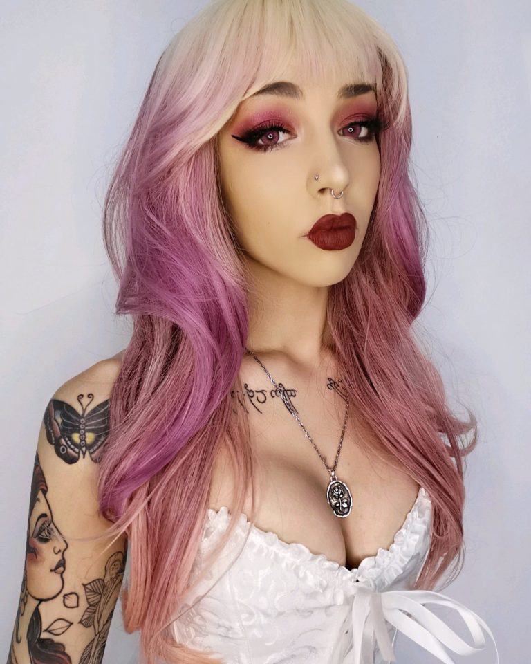 A sleek mid length wig finished in a blow out for body and volume. Creamy blonde roots melt into a muted rose pink. With a sleek blonde blunt fringe.