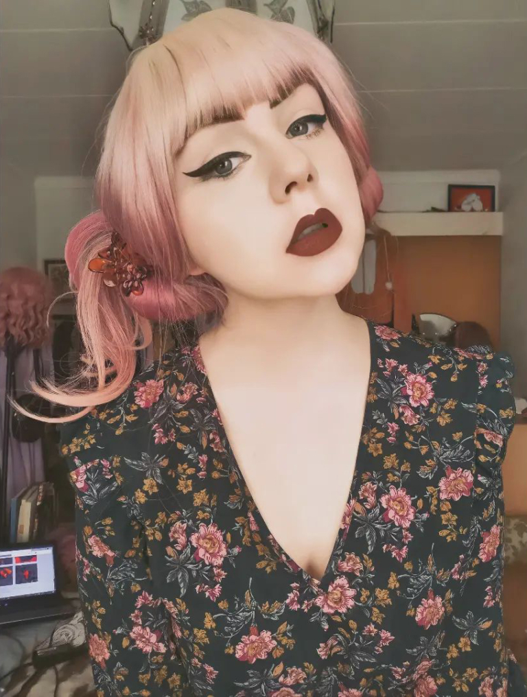 A sleek mid length wig finished in a blow out for body and volume. Creamy blonde roots melt into a muted rose pink. With a sleek blonde blunt fringe.