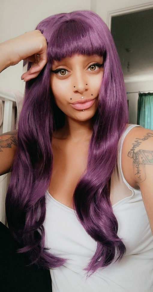Purple long curly lace front wig with bangs. A rich, jewel toned purple hue. The cut is long and finished with loose curls. This is our only lace front with a full fringe. Deep Purple looks vibrant paired with bright looks or striking with dark monochrome outfits.