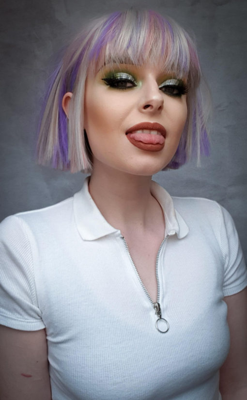 Hina - Lush Wigs UK Silver grey bob wig with bangs. Hina is a striking colour block A-line bob, with matching choppy blunt fringe. A silvery grey shade dominates, but brought to life with baby pink and purple pastel highlights running through it. A sleek and blunt style carries this distinctive look.