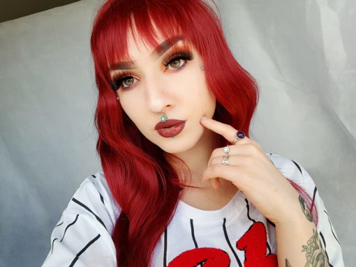 Red long wavy wig with bangs. Temptation is rich and vibrant. Deep chilli red from roots to tips. This style is cut into long invisible layers, gentle waves runs throughout the lengths that fall to the hips. A choppy fringe finishes the look.