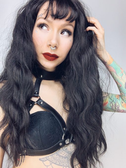 Black long wavy wig with bangs. Conjure some gothic glamour with Apparition. Warm black tone with long loose curls with invisible layers to add body and movement to the look.