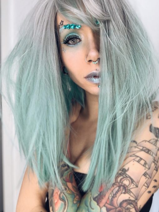 Silvery grey roots with a minty green ombre, this gorgeous wig has a hidden pop of blue in the back! With a blunt wispy fringe and a realistic skin top parting, this one is the perfect way to try bright hair while maintaining a natural style.