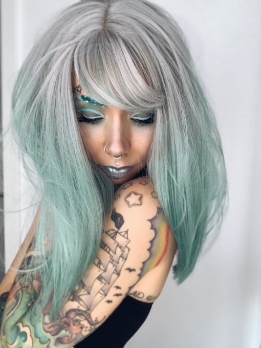 Silvery grey roots with a minty green ombre, this gorgeous wig has a hidden pop of blue in the back! With a blunt wispy fringe and a realistic skin top parting, this one is the perfect way to try bright hair while maintaining a natural style.