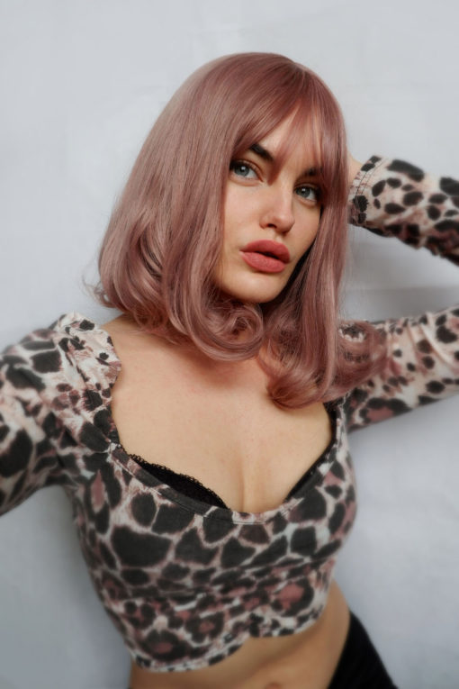 Dusty pink bob wig with bangs. This sweet and feminine style, Dusky pink tones from roots to tips, that nods to rose gold hues. That fall to the shoulders. Complete with fringe and finished with a gentle curl under.