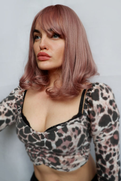 Dusty pink bob wig with bangs. This sweet and feminine style, Dusky pink tones from roots to tips, that nods to rose gold hues. That fall to the shoulders. Complete with fringe and finished with a gentle curl under.