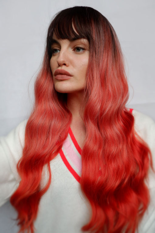 Orange ombre long wavy wig with bangs. Papaya takes on colour dimensions. Dark brown roots and fringe that melt into a washed-out orange tone. Finished with vibrant orange tones for a dip-dyed effect. A barely there wave generates an illusion of fullness.