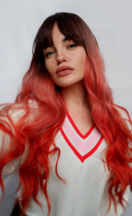 Orange ombre long wavy wig with bangs. Papaya takes on colour dimensions. Dark brown roots and fringe that melt into a washed-out orange tone. Finished with vibrant orange tones for a dip-dyed effect. A barely there wave generates an illusion of fullness.