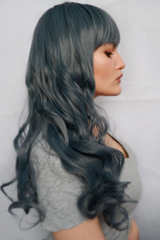 Deep, unusual denim blue. We love this stunning style, sleek around the face and then wavy curls finish off the lengths, topped with a thick, choppy fringe. This wig has a closure top, and falls above the bust.