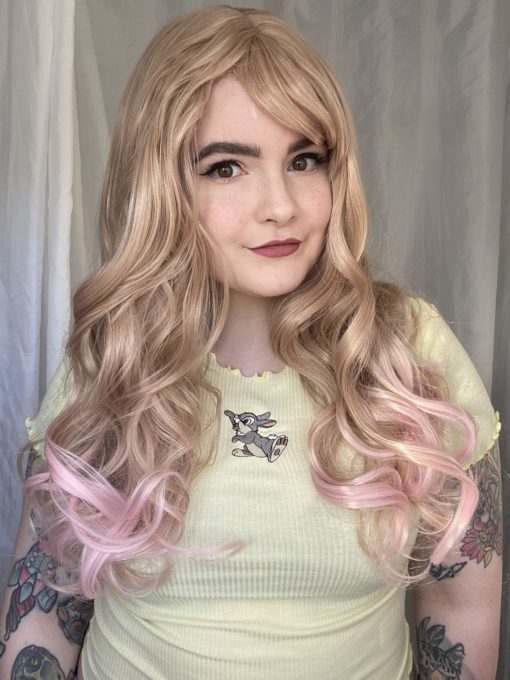Blonde to pastel pink ombre wig. Choux is styled into cascading curls with a sleek fringe. This creamy blonde tone melts into a baby pink.