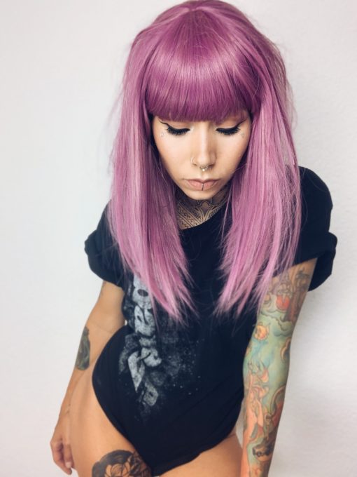 Light purple long wig with bangs. Azalea takes on a combination of pinks and purples in this colour mix from roots to tips. Straight and sleek lengths ending just below the shoulders. A versatile style and easy to maintain. An instant head turner.