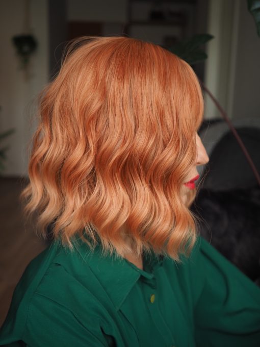 Mara is a mix of coral and light blonde tones that deliver a beautiful natural ginger hue. With a creamy peach dip dye effect on the ends. The style carries a defined wave that falls just above the shoulders, with a sleek fringe.