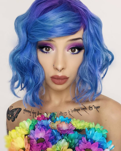 Blue wavy bob wig with bangs. Blueberry takes a mixture of pastel tones. A light pinky-purple dyes the roots and wispy fringe, that melt into a sky blue colour. Beachy waves give texture and body, falling just above the shoulders.