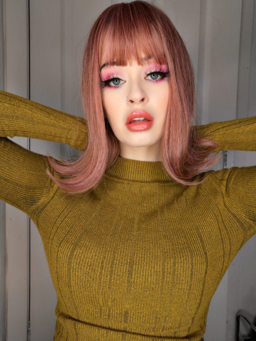 Pink straight bob wig with bangs. Deelite is Pretty and alluring with its unusual colour. A mix of ginger and pink hues that create a beautiful rose gold colour. A long bob with a classic sixties flick at the ends. Just dances above the shoulders. Full fringe to frame the face.