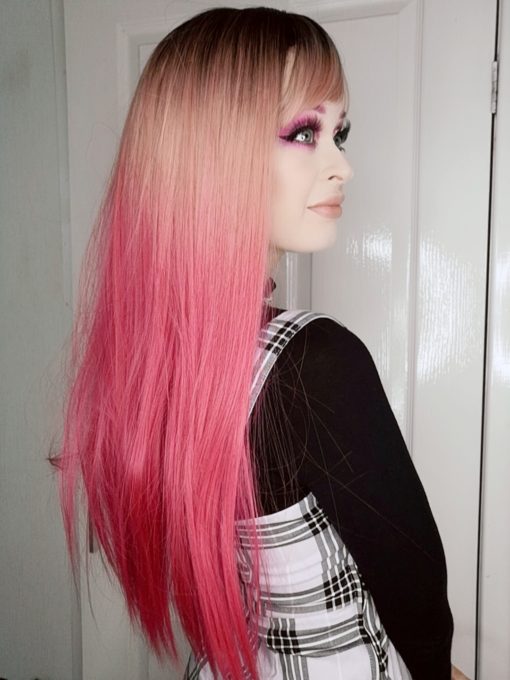 Pink ombre long straight wig with dark roots. Kyandi creates an unusual mixture of dark grey roots that melt into a dusky pink, blends to a magenta pink that dominates the sleek length of this style.