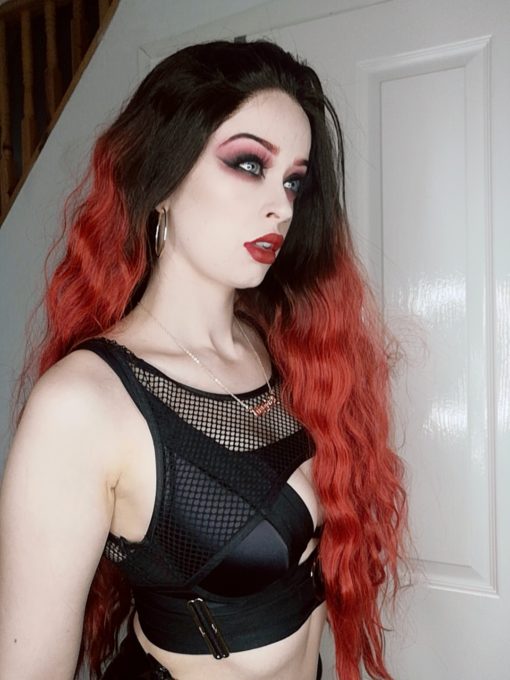 Bright red long wavy lace front wig with dark roots. This big vibrant style takes centre stage, with black roots that flows into an ombre of red hues. Finished in crimped waves that falls to the hips in layers for texture.