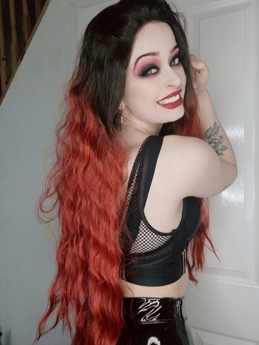 Bright red long wavy lace front wig with dark roots. This big vibrant style takes centre stage, with black roots that flows into an ombre of red hues. Finished in crimped waves that falls to the hips in layers for texture.