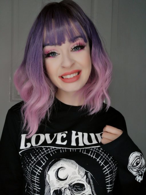 Purple and pink, long wavy bob wig with bangs. Sugarpop takes on colour dimensions, this pretty colour mix of cool brown shadowed roots, that become a soft purple ombre colour around the crown of the head and in the fringe. Melting into a light pink dip dye ends.