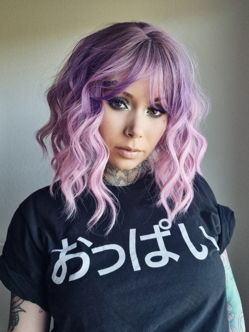 This wig has brown shadowed roots that melt into a dark lilac colour into a soft pink ombre. A bob styled into loose waves with a sleek blunt fringe.
