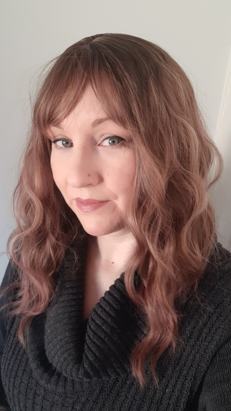 This wig has brown shadowed roots that blend into a mix of warm chocolate browns and dark pinks. They create this beautiful rosewood colour. Styled in a loose wave with subtle layers. The light fringe is sleek and blunt.