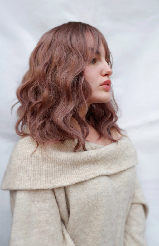Yoake is a long bob (lob) with brown shadow roots that run into the fringe to frame the face. We love the mix of warm chocolate browns and dark pinks to create this beautiful rosewood colour. Dishevelled waves fall just to the collarbones.