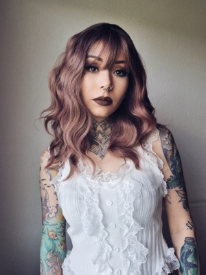 This wig has brown shadowed roots that blend into a mix of warm chocolate browns and dark pinks. They create this beautiful rosewood colour. Styled in a loose wave with subtle layers. The light fringe is sleek and blunt.