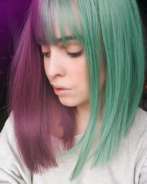 Purple and green split long bob wig. Ripley takes on the dramatic colour divide. This bright and bold sci-fi inspired style, has a plum shade paired with a dark emerald colour Split down the centre parting and carrying the colour through the fringe. Styled straight with plenty of volume that curls at the tips, falling just below the shoulders. Easy to wear and maintain.