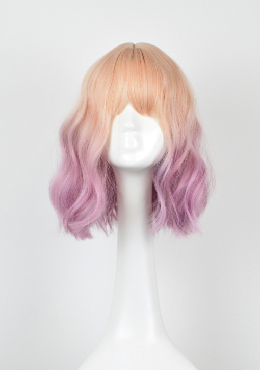Blonde and pink wavy bob wig with bangs. Buttercup has a natural twist of vanilla roots that carry a washed-out pastel pink. Styled in loose waves to give texture and body, with a wispy fringe to frame the face.