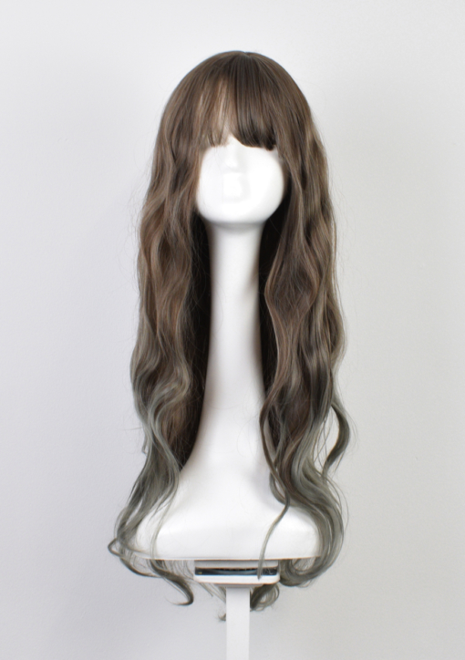 Brown and green wavy wig with bangs. Pistachio has a subtle mixture of brown and sage colours to create a silvery tone throughout the lengths. Finished with a light sage dip dye on the ends. 