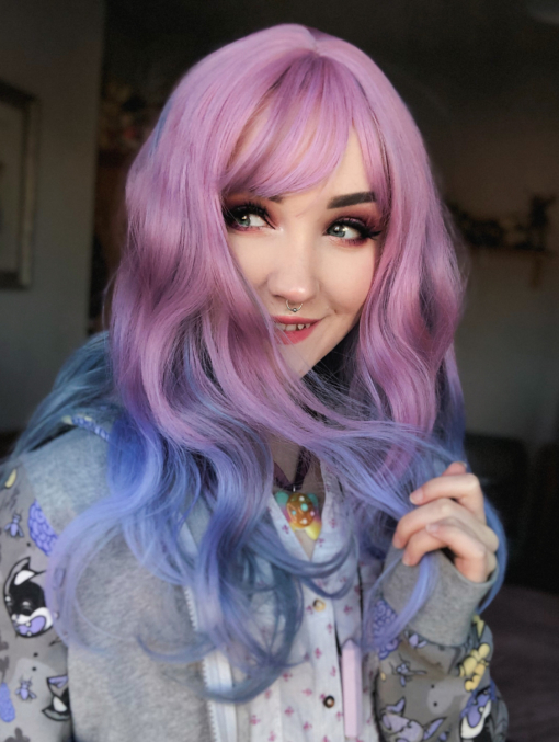 Pink and blue ombre long wavy wig with bangs. Bluebell nails it, a perfect blend of pastel pink from the roots, melting into a pale blue ombre. Delicate waves and a wispy fringe.