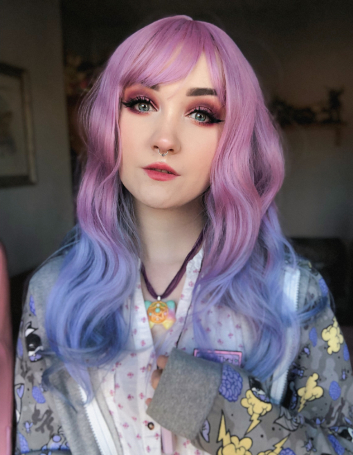 Pink and blue ombre long wavy wig with bangs. Bluebell nails it, a perfect blend of pastel pink from the roots, melting into a pale blue ombre. Delicate waves and a wispy fringe.