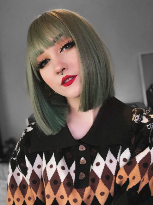 Green straight bob with bangs. Fern is a natural twist of sage. This super poker straight bob has a soft and natural feel, yet the colour gives a grungy feel to the style. A blunt fringe frames the face.
