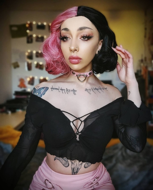 Pink and black split wavy bob wig with bangs. Thura takes on the dramatic colour divide. A rose pink and black colour, split down the centre parting the colour that falls each side of the face. Sleek from the roots with soft 60s flick curl at the ends.