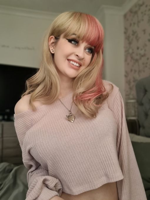 Zarita - Lush Wigs UK Blonde and pink long wavy wig with bangs. Zarita is a sandy blonde colour with a chunky block of pink flamingo hue running down the one side of the style, that runs into half of the fringe. This style doesn't disappoint. Wear it as a pop of colour, or mess it up. Good for those who are new to wigs, as it's easy to wear and maintain.