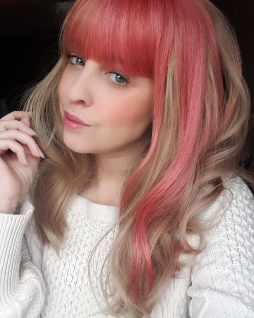 Zarita - Lush Wigs UK Blonde and pink long wavy wig with bangs. Zarita is a sandy blonde colour with a chunky block of pink flamingo hue running down the one side of the style, that runs into half of the fringe. This style doesn't disappoint. Wear it as a pop of colour, or mess it up. Good for those who are new to wigs, as it's easy to wear and maintain.